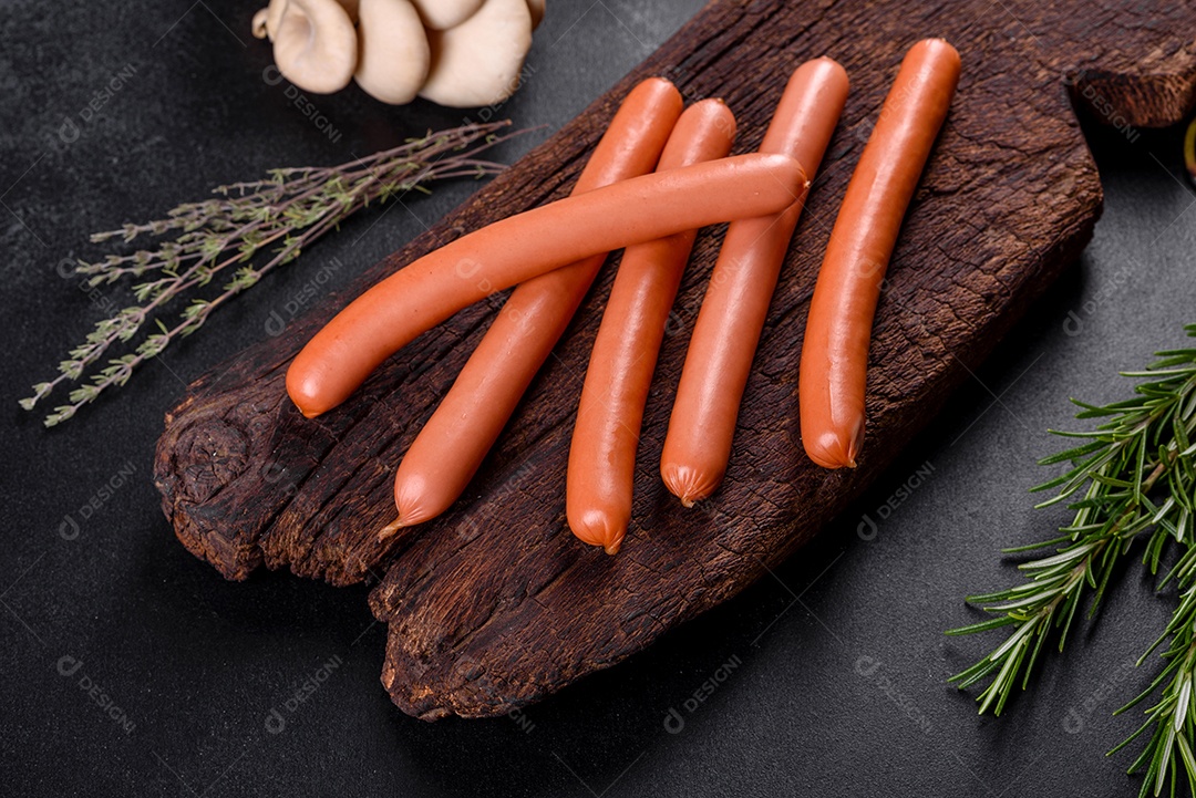 Salsichas cozidas em uma tábua de madeira sobre um fundo escuro de concreto. Alimentos não saudáveis