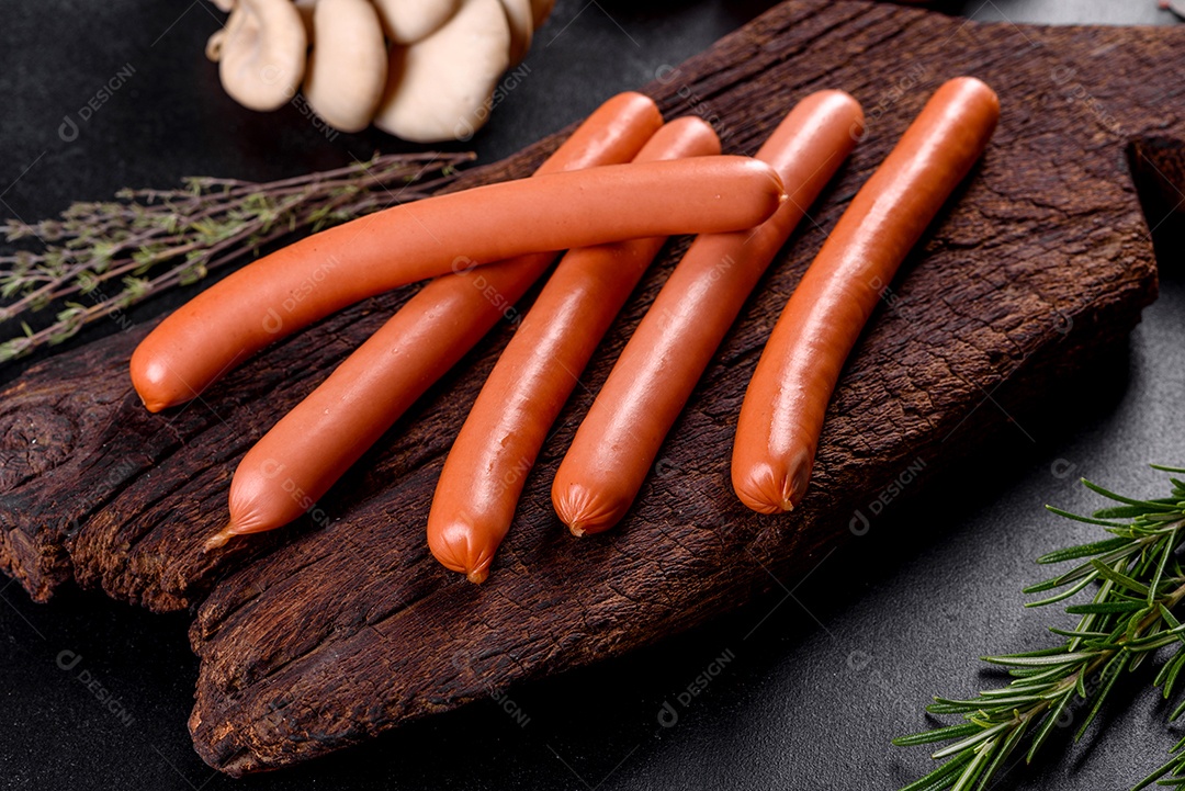 Salsichas cozidas em uma tábua de madeira sobre um fundo escuro de concreto. Alimentos não saudáveis