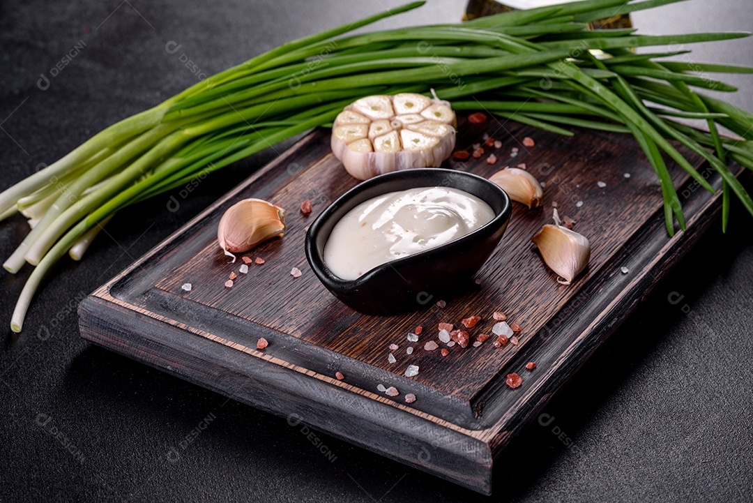 Molho de alho em molho preto cerâmico com vegetação em uma tábua de madeira sobre uma mesa de concreto escuro