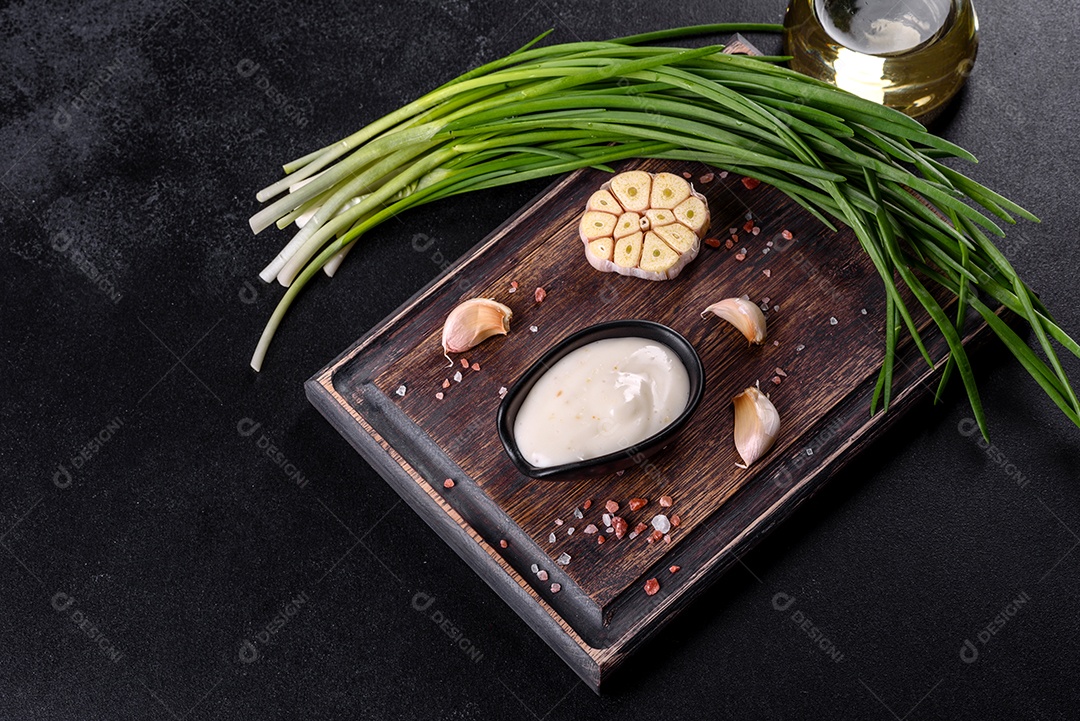 Molho de alho em molho preto cerâmico com vegetação em uma tábua de madeira sobre uma mesa de concreto escuro