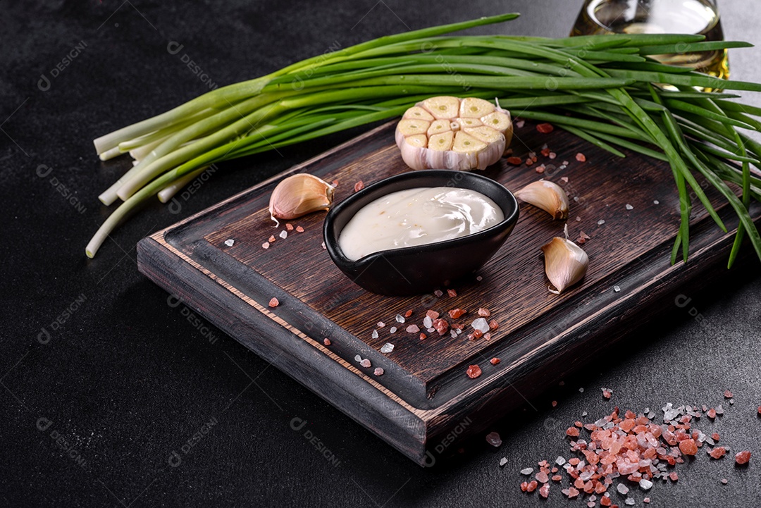 Molho de alho em molho preto cerâmico com vegetação em uma tábua de madeira sobre uma mesa de concreto escuro