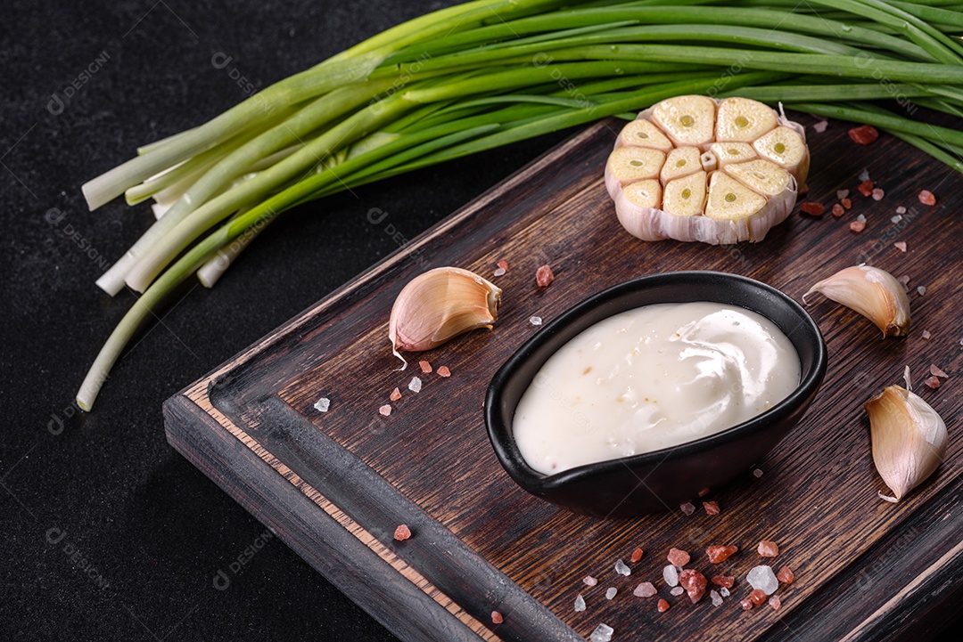 Molho de alho em molho preto cerâmico com vegetação em uma tábua de madeira sobre uma mesa de concreto escuro