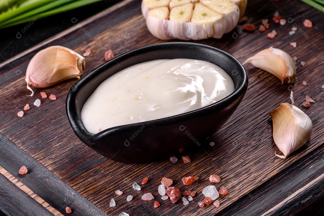 Molho de alho em molho preto cerâmico com vegetação em uma tábua de madeira sobre uma mesa de concreto escuro