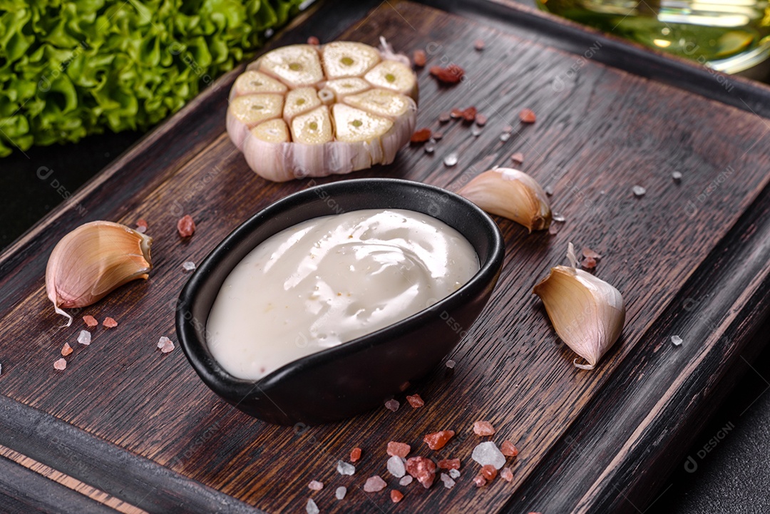 Molho de alho em molho preto cerâmico com vegetação em uma tábua de madeira sobre uma mesa de concreto escuro