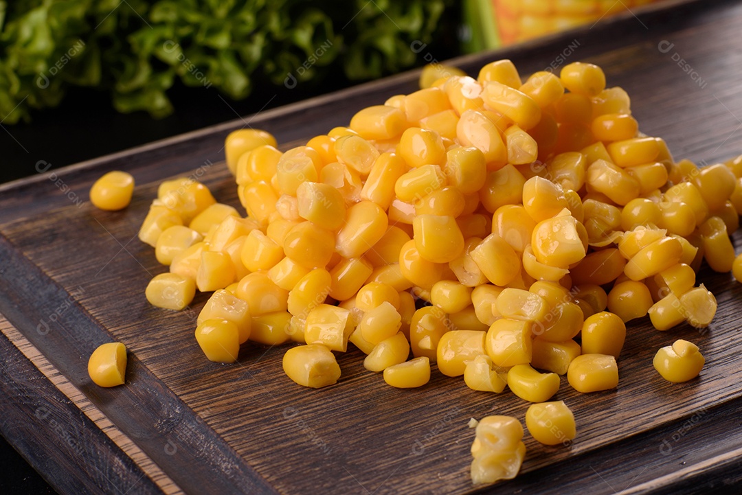Milho enlatado fresco e delicioso em uma tábua de madeira sobre um fundo escuro de concreto