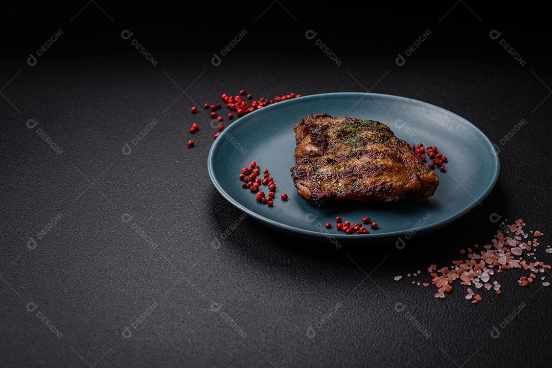 Delicioso bife suculento ou bife de frango com sal, especiarias e ervas sobre um fundo escuro de concreto