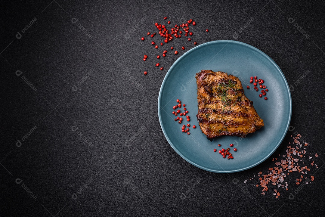 Delicioso bife suculento ou bife de frango com sal, especiarias e ervas sobre um fundo escuro de concreto