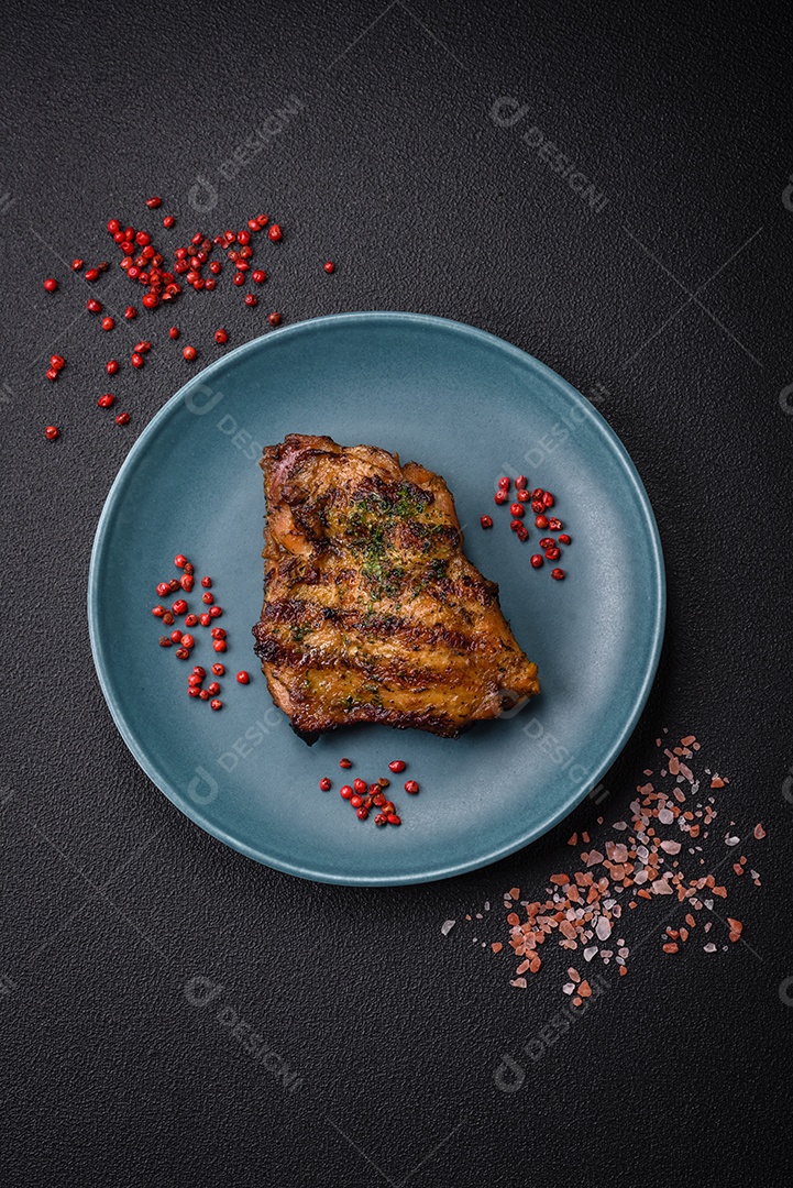 Delicioso bife suculento ou bife de frango com sal, especiarias e ervas sobre um fundo escuro de concreto