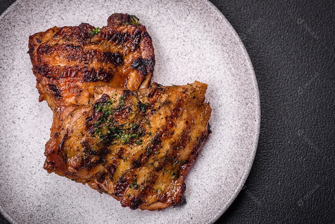 Delicioso bife suculento ou bife de frango com sal, especiarias e ervas sobre um fundo escuro de concreto
