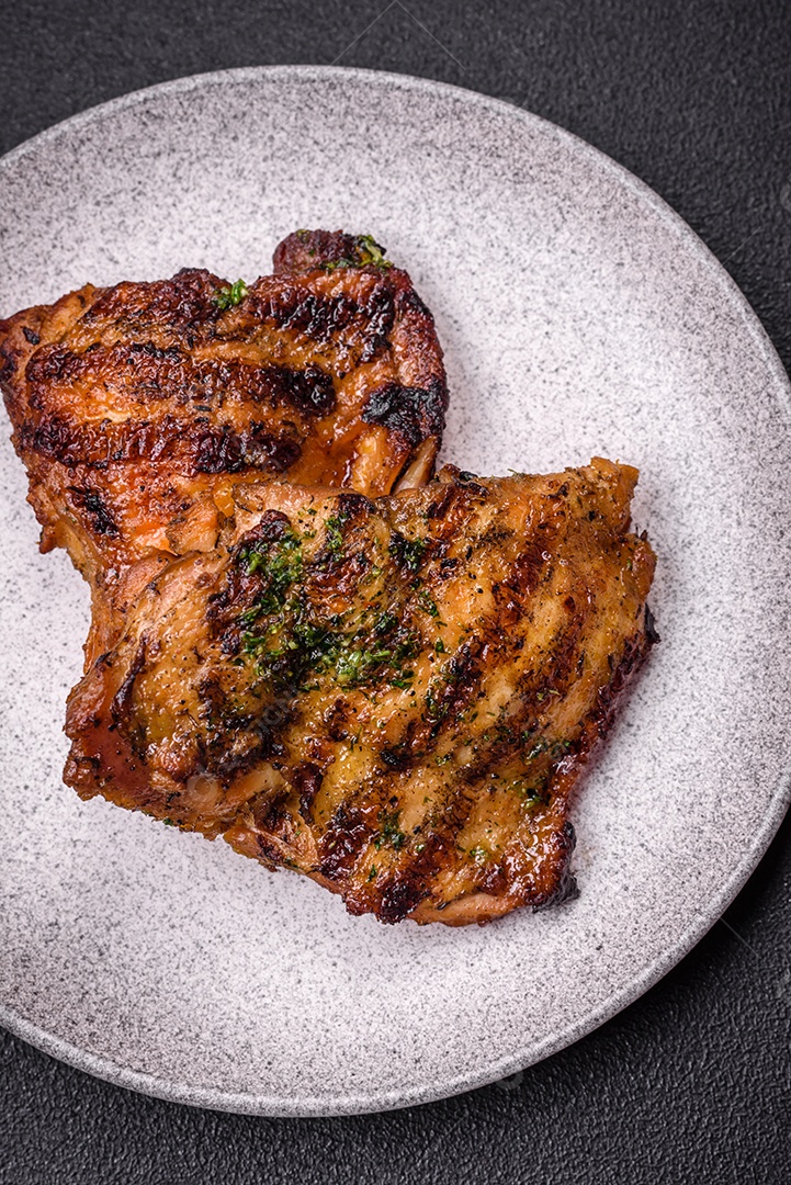 Delicioso bife suculento ou bife de frango com sal, especiarias e ervas sobre um fundo escuro de concreto