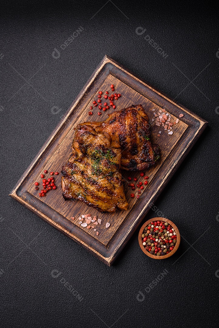 Delicioso bife suculento ou bife de frango com sal, especiarias e ervas sobre um fundo escuro de concreto