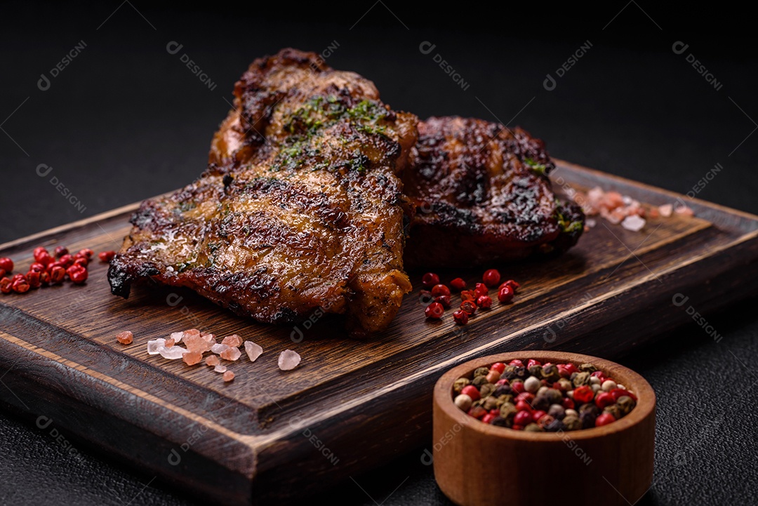 Delicioso bife suculento ou bife de frango com sal, especiarias e ervas sobre um fundo escuro de concreto