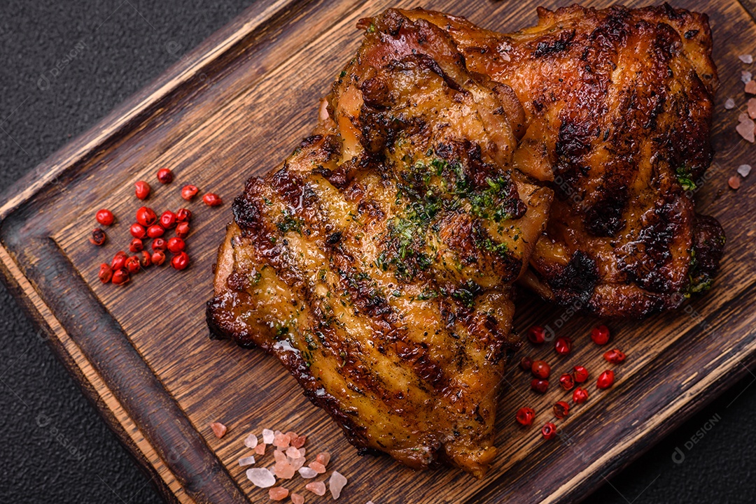 Delicioso bife suculento ou bife de frango com sal, especiarias e ervas sobre um fundo escuro de concreto
