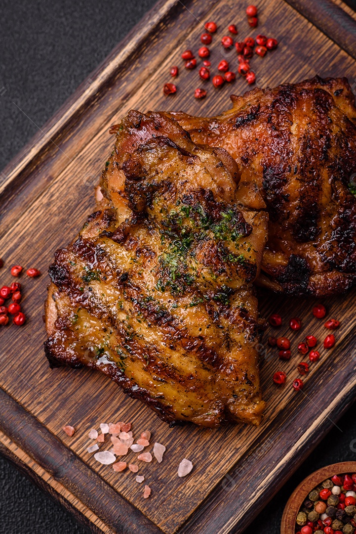 Delicioso bife suculento ou bife de frango com sal, especiarias e ervas sobre um fundo escuro de concreto