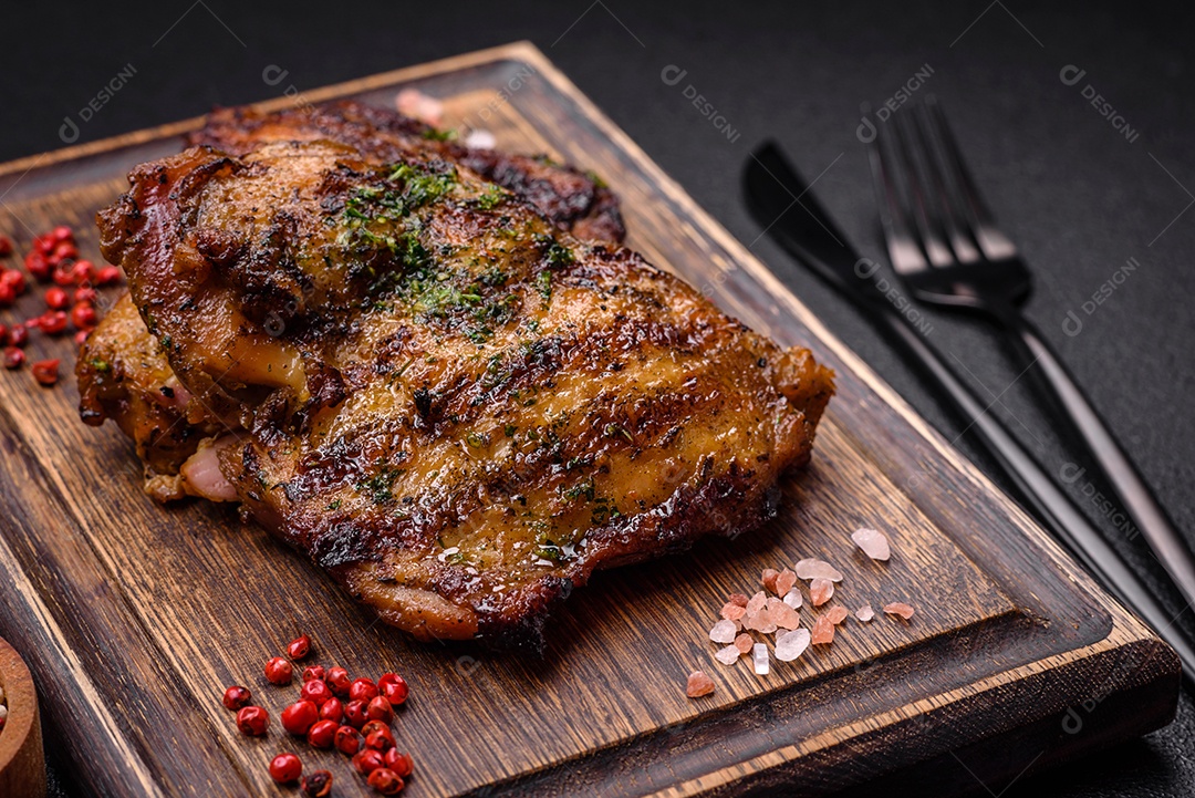 Delicioso bife suculento ou bife de frango com sal, especiarias e ervas sobre um fundo escuro de concreto