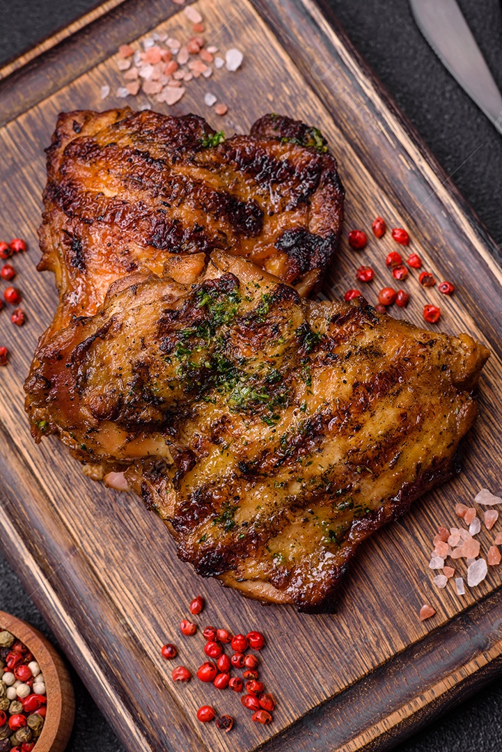 Delicioso bife suculento ou bife de frango com sal, especiarias e ervas sobre um fundo escuro de concreto
