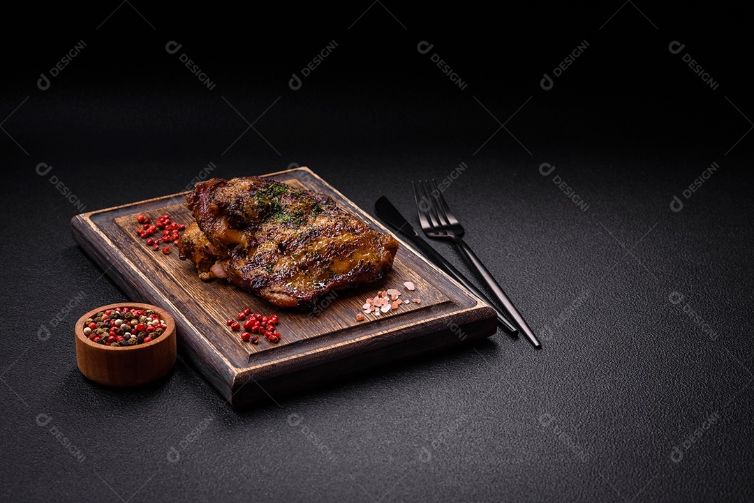 Delicioso bife suculento ou bife de frango com sal, especiarias e ervas sobre um fundo escuro de concreto