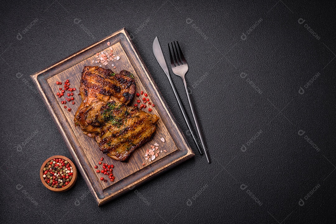 Delicioso bife suculento ou bife de frango com sal, especiarias e ervas sobre um fundo escuro de concreto