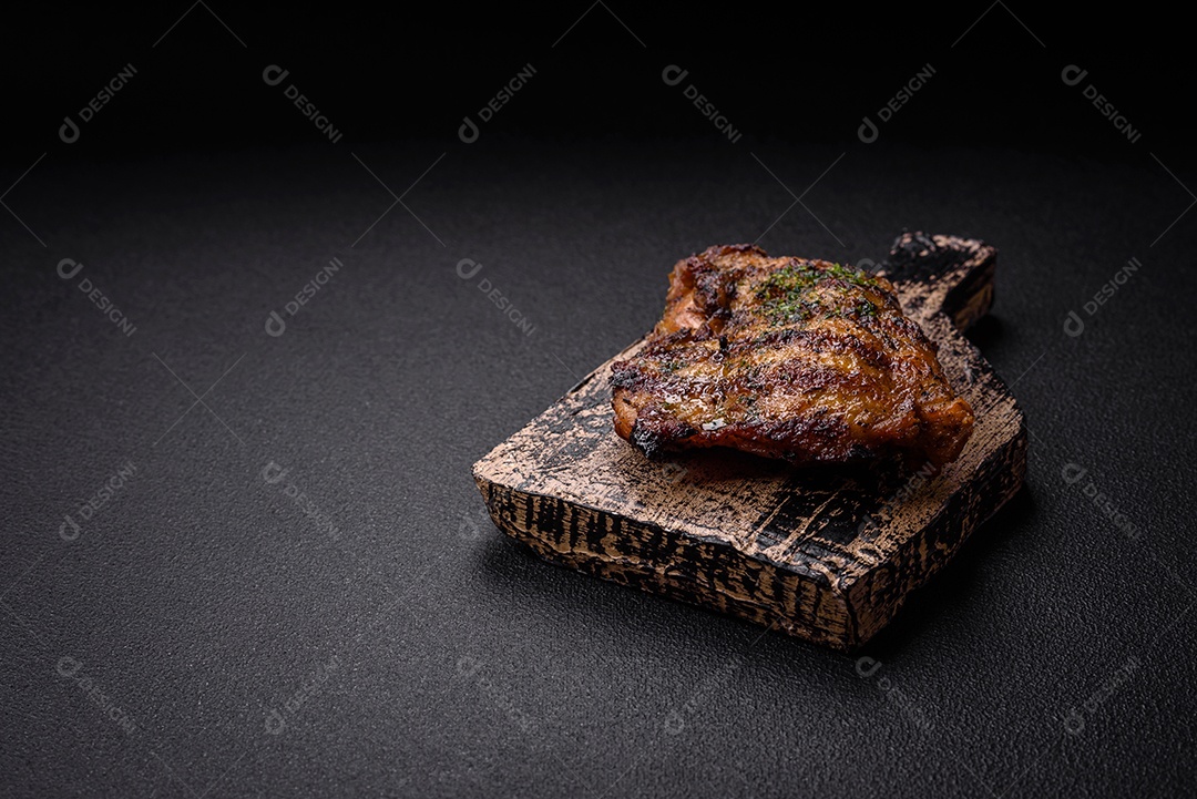 Delicioso bife suculento ou bife de frango com sal, especiarias e ervas sobre um fundo escuro de concreto