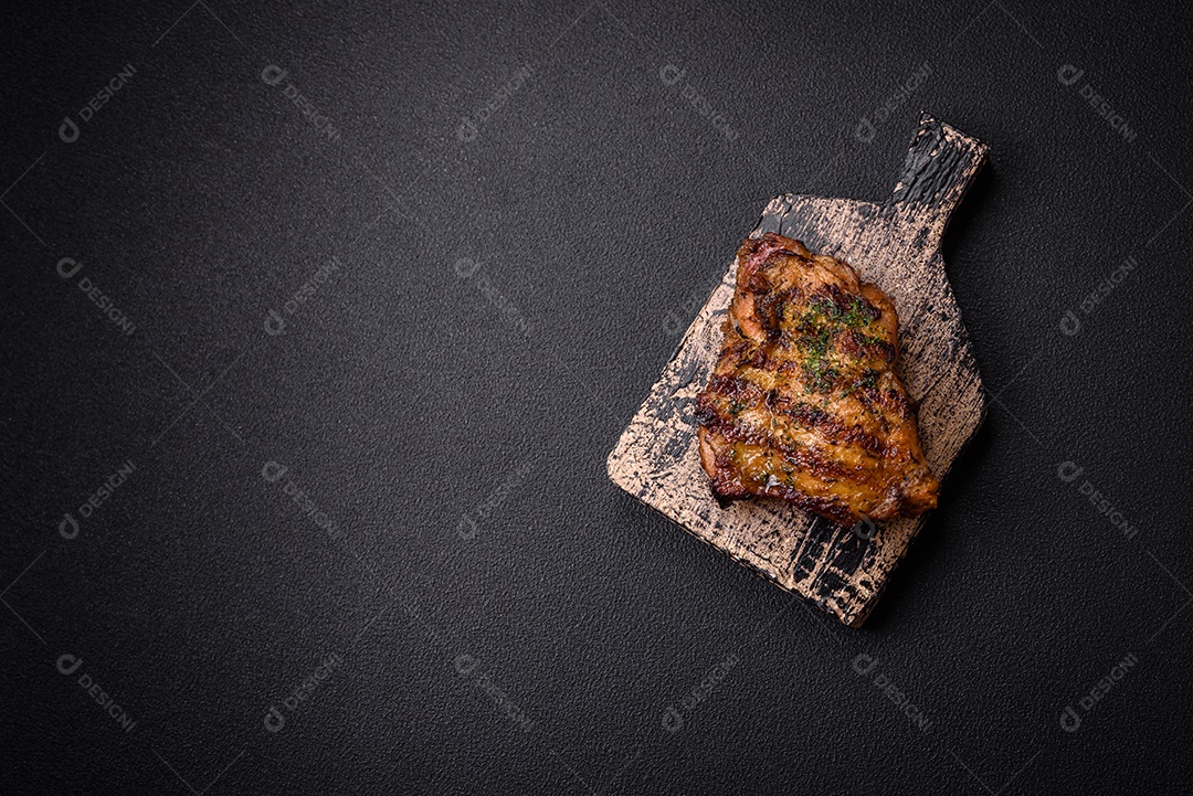 Delicioso bife suculento ou bife de frango com sal, especiarias e ervas sobre um fundo escuro de concreto