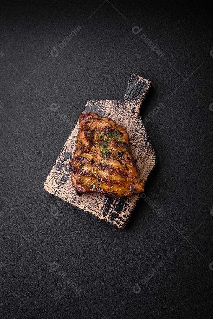 Delicioso bife suculento ou bife de frango com sal, especiarias e ervas sobre um fundo escuro de concreto