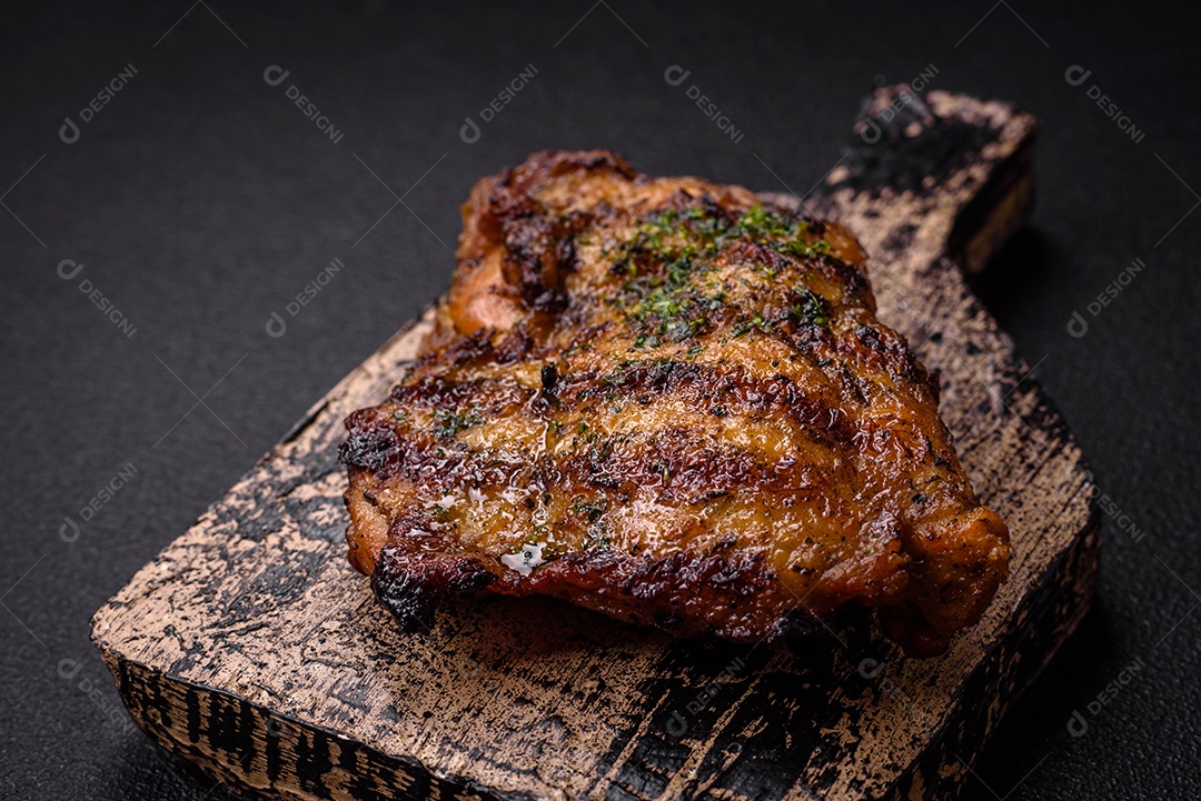 Delicioso bife suculento ou bife de frango com sal, especiarias e ervas sobre um fundo escuro de concreto