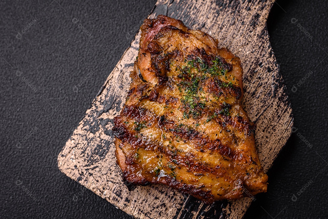 Delicioso bife suculento ou bife de frango com sal, especiarias e ervas sobre um fundo escuro de concreto