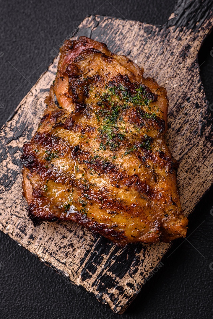 Delicioso bife suculento ou bife de frango com sal, especiarias e ervas sobre um fundo escuro de concreto