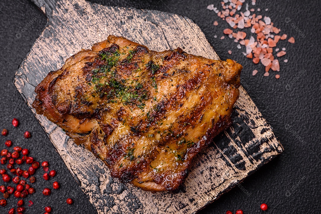 Delicioso bife suculento ou bife de frango com sal, especiarias e ervas sobre um fundo escuro de concreto