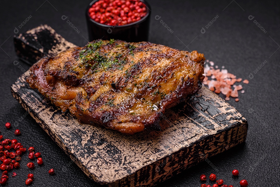Delicioso bife suculento ou bife de frango com sal, especiarias e ervas sobre um fundo escuro de concreto