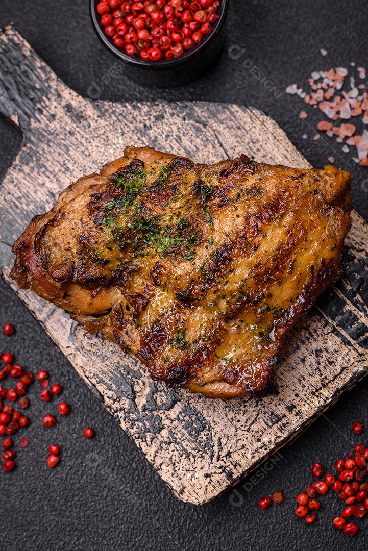 Delicioso bife suculento ou bife de frango com sal, especiarias e ervas sobre um fundo escuro de concreto
