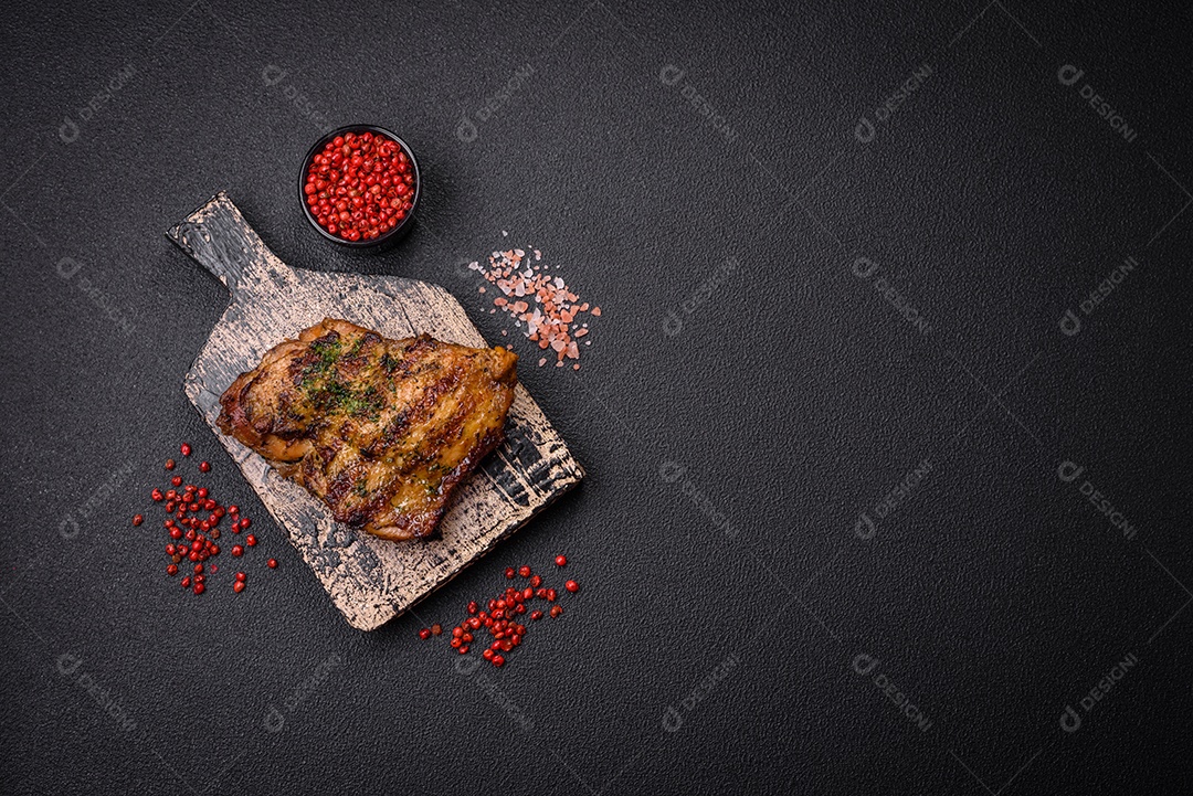 Delicioso bife suculento ou bife de frango com sal, especiarias e ervas sobre um fundo escuro de concreto