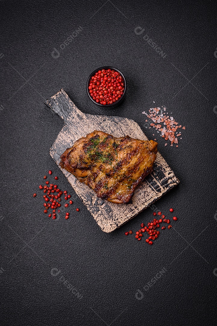 Delicioso bife suculento ou bife de frango com sal, especiarias e ervas sobre um fundo escuro de concreto