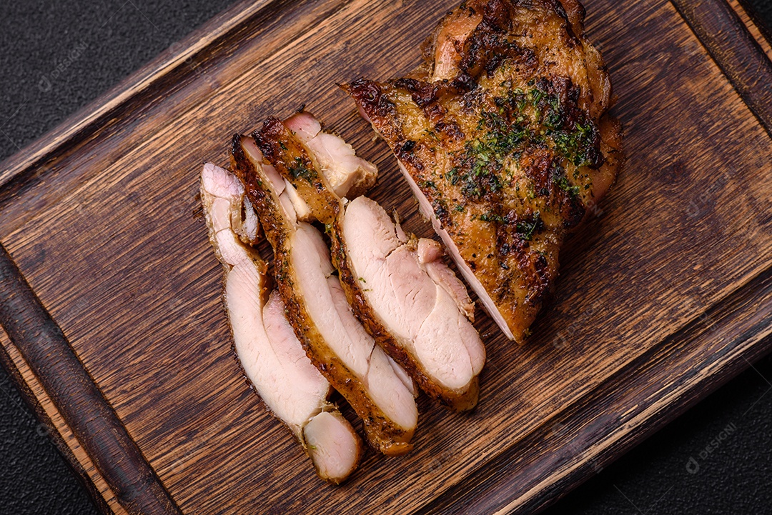 Delicioso bife suculento ou bife de frango com sal, especiarias e ervas sobre um fundo escuro de concreto