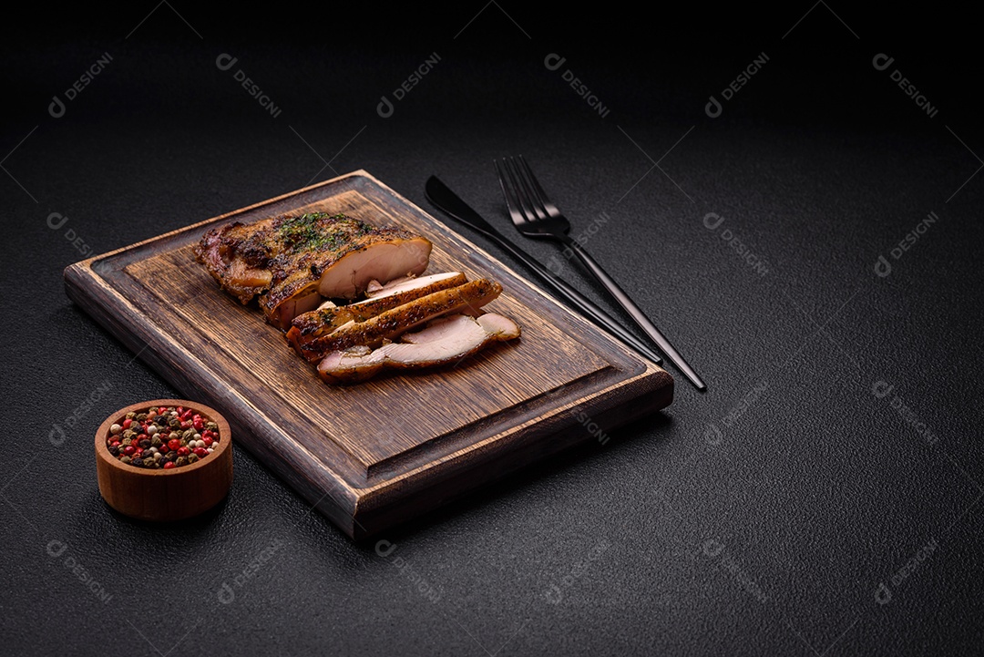 Delicioso bife suculento ou bife de frango com sal, especiarias e ervas sobre um fundo escuro de concreto