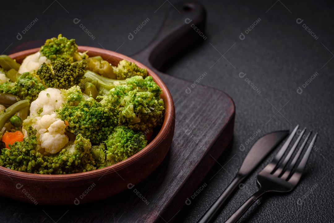 Deliciosos legumes frescos cozidos cenouras, brócolis, couve-flor em uma placa preta sobre um fundo escuro de concreto
