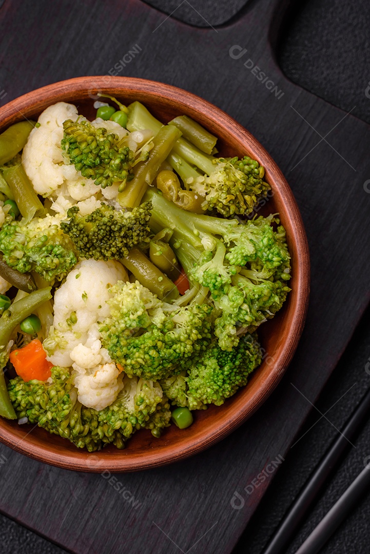 Deliciosos legumes frescos cozidos cenouras, brócolis, couve-flor em uma placa preta sobre um fundo escuro de concreto