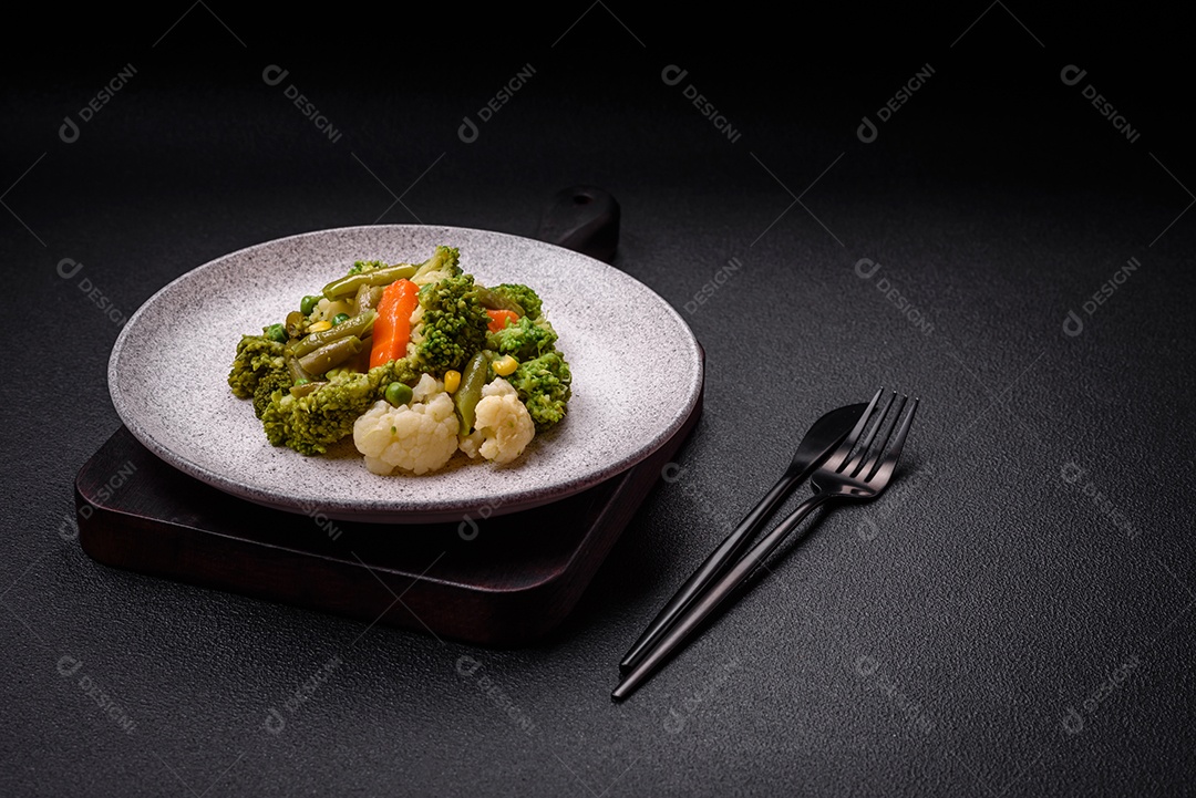 Deliciosos legumes frescos cozidos cenouras, brócolis, couve-flor em uma placa preta sobre um fundo escuro de concreto