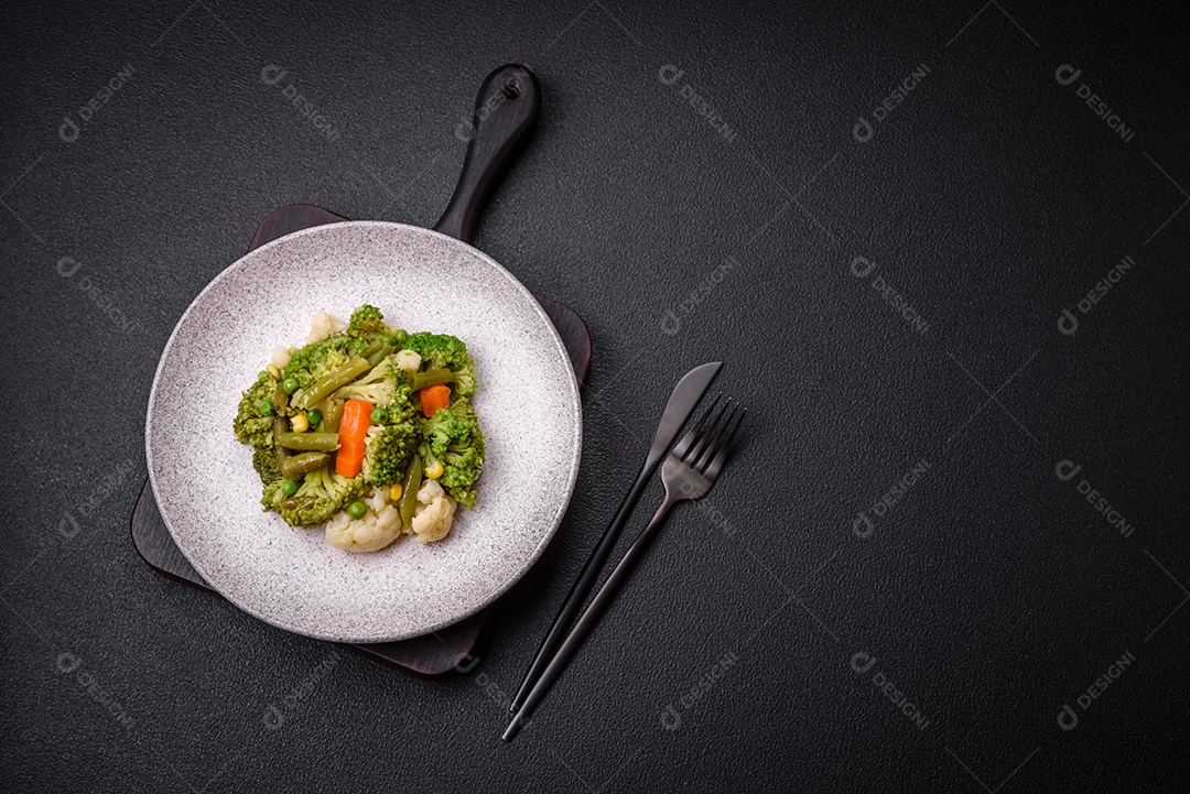 Deliciosos legumes frescos cozidos cenouras, brócolis, couve-flor em uma placa preta sobre um fundo escuro de concreto