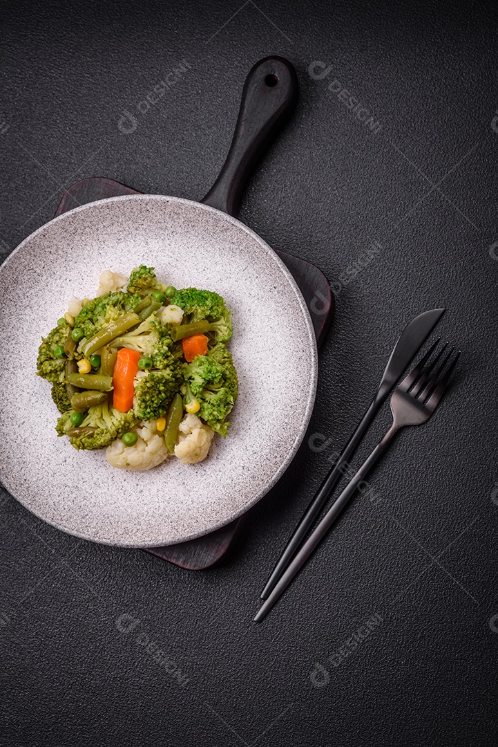 Deliciosos legumes frescos cozidos cenouras, brócolis, couve-flor em uma placa preta sobre um fundo escuro de concreto
