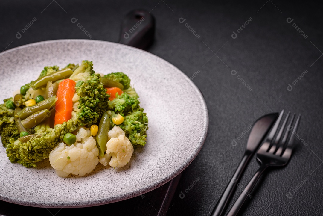 Deliciosos legumes frescos cozidos cenouras, brócolis, couve-flor em uma placa preta sobre um fundo escuro de concreto