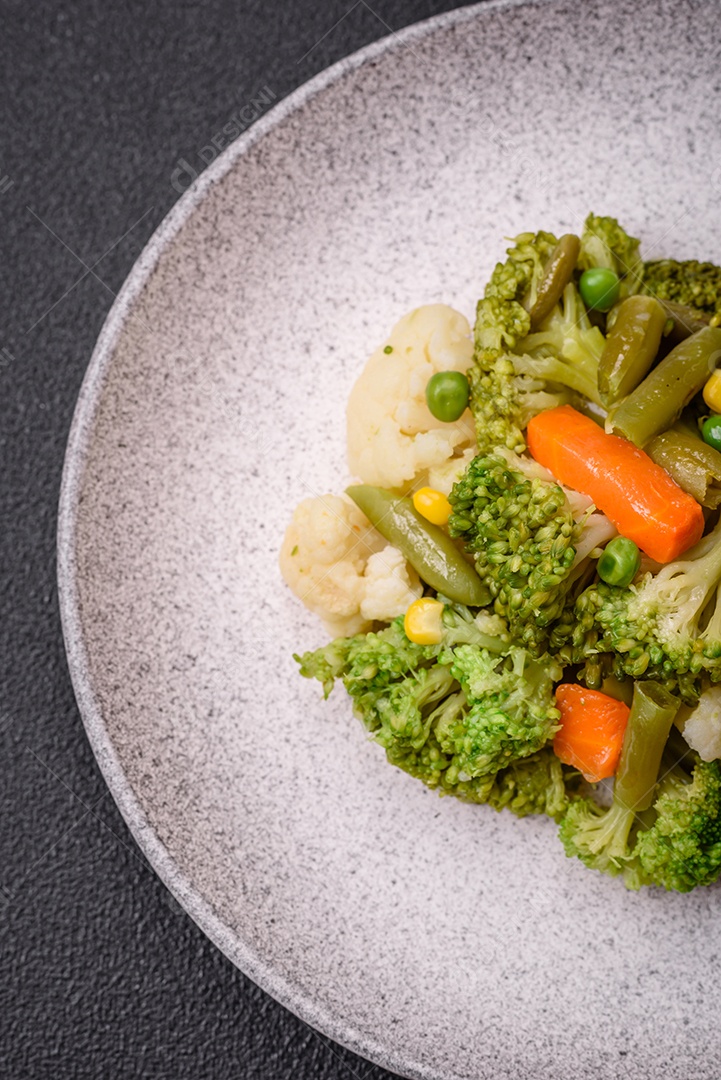 Deliciosos legumes frescos cozidos cenouras, brócolis, couve-flor em uma placa preta sobre um fundo escuro de concreto