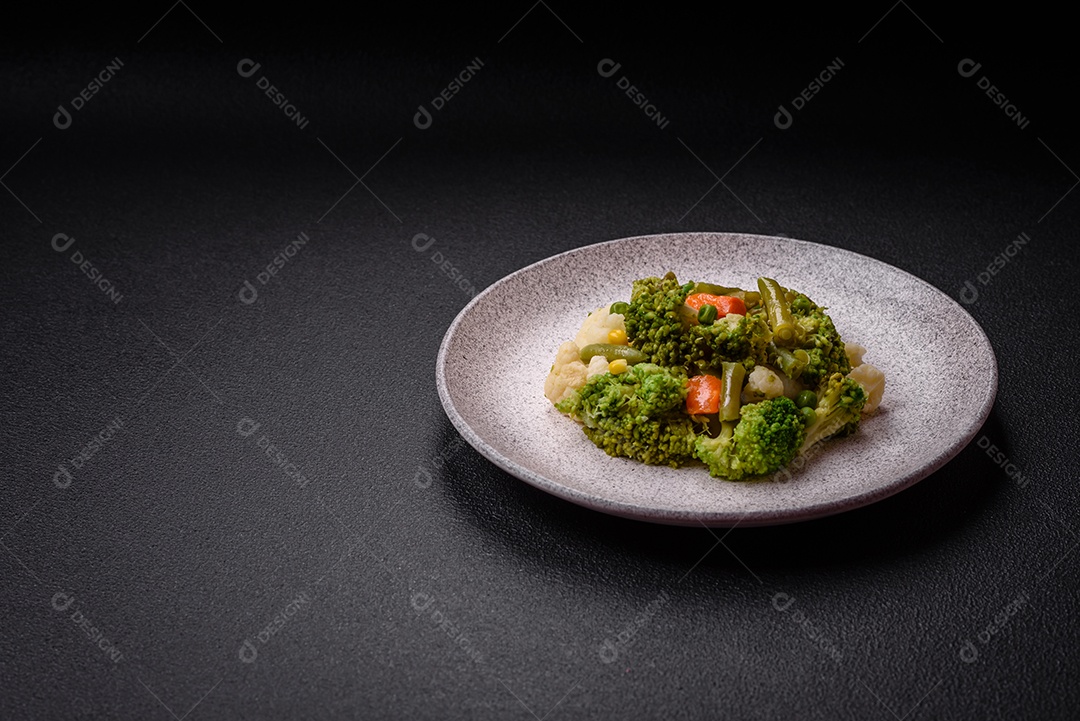 Deliciosos legumes frescos cozidos cenouras, brócolis, couve-flor em uma placa preta sobre um fundo escuro de concreto