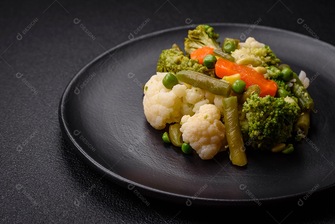 Deliciosos legumes frescos cozidos cenouras, brócolis, couve-flor em uma placa preta sobre um fundo escuro de concreto