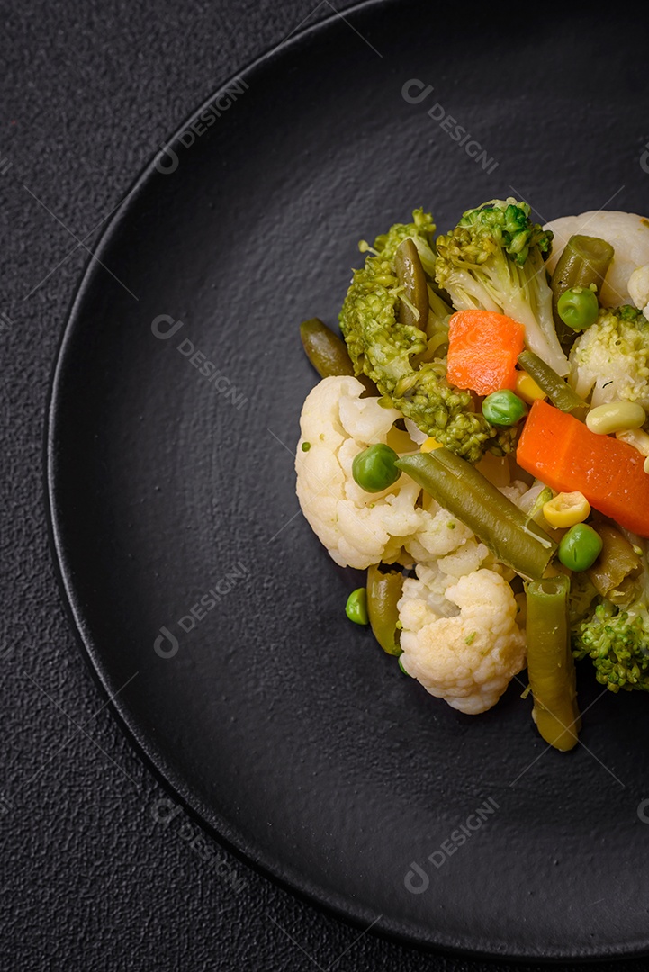 Deliciosos legumes frescos cozidos cenouras, brócolis, couve-flor em uma placa preta sobre um fundo escuro de concreto