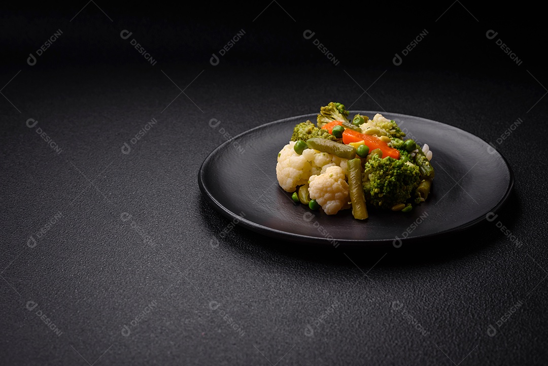 Deliciosos legumes frescos cozidos cenouras, brócolis, couve-flor em uma placa preta sobre um fundo escuro de concreto