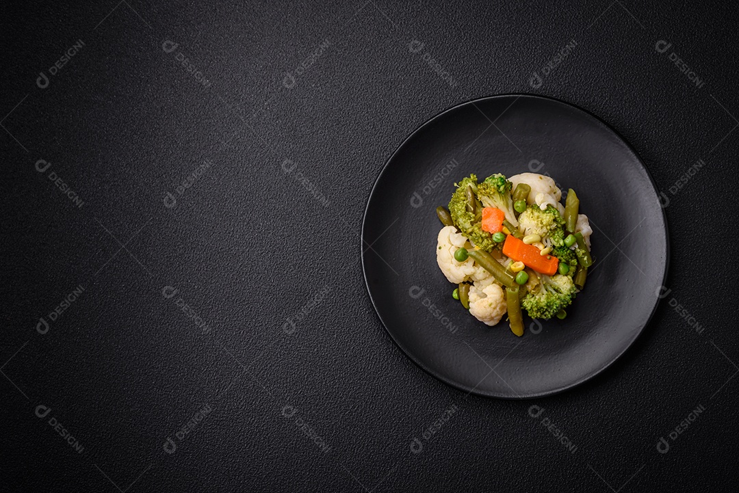 Deliciosos legumes frescos cozidos cenouras, brócolis, couve-flor em uma placa preta sobre um fundo escuro de concreto