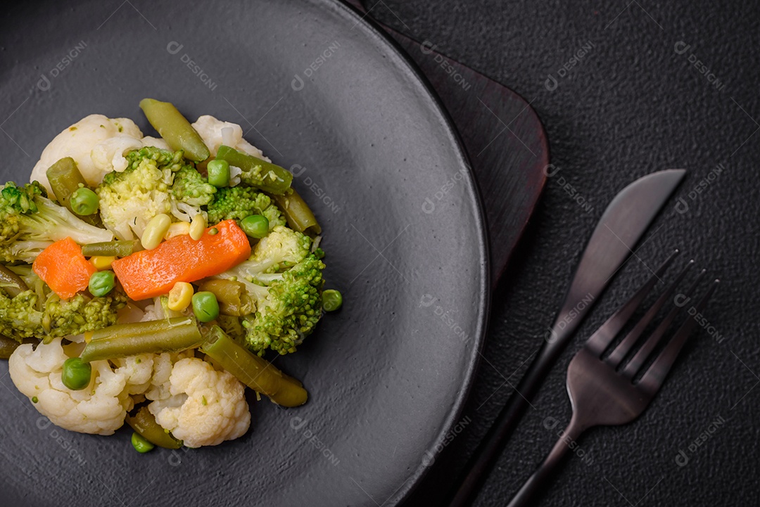 Deliciosos legumes frescos cozidos cenouras, brócolis, couve-flor em uma placa preta sobre um fundo escuro de concreto