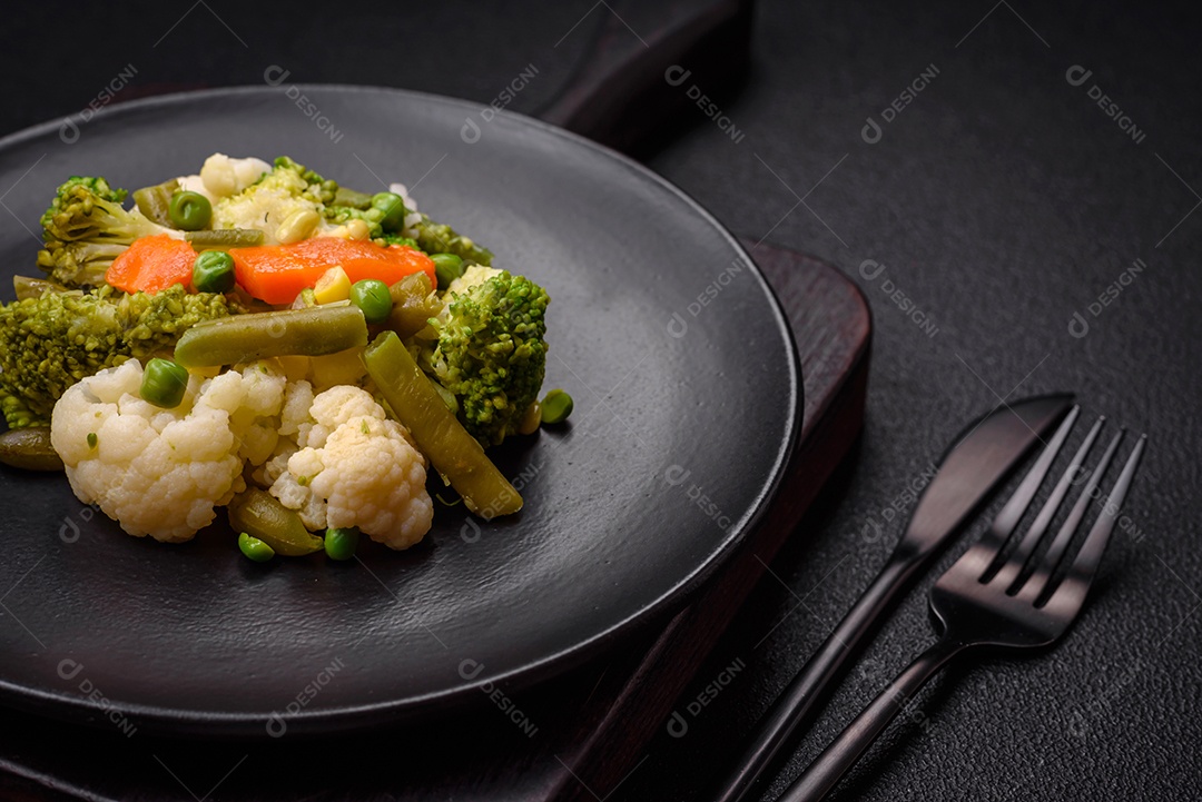 Deliciosos legumes frescos cozidos cenouras, brócolis, couve-flor em uma placa preta sobre um fundo escuro de concreto