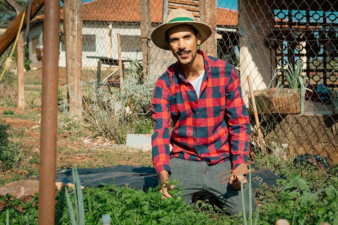 Agricultor de chapéu analisando a plantação ao pôr do sol